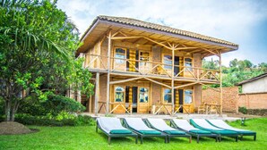 A wooden building with a balcony and a covered outdoor seating area with lounge chairs. - Paradis Malahide (Nyayumba)