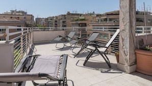 A rooftop terrace with sun loungers, a railing, and a view of surrounding buildings. - GuestHost - Cozy and comfortable 75sqm apartment, able to accommodate up to 6 people, located on the 5th floor with elevator (not suitable for disabled peolple) of a building less than 10 minutes walk away from Bologna Metro stop and the homonymous squ (Roma)