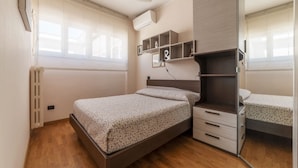 A bedroom with a bed, a wardrobe, a mirror, and a window. - GuestHost - Cozy and comfortable 75sqm apartment, able to accommodate up to 6 people, located on the 5th floor with elevator (not suitable for disabled peolple) of a building less than 10 minutes walk away from Bologna Metro stop and the homonymous squ (Roma)