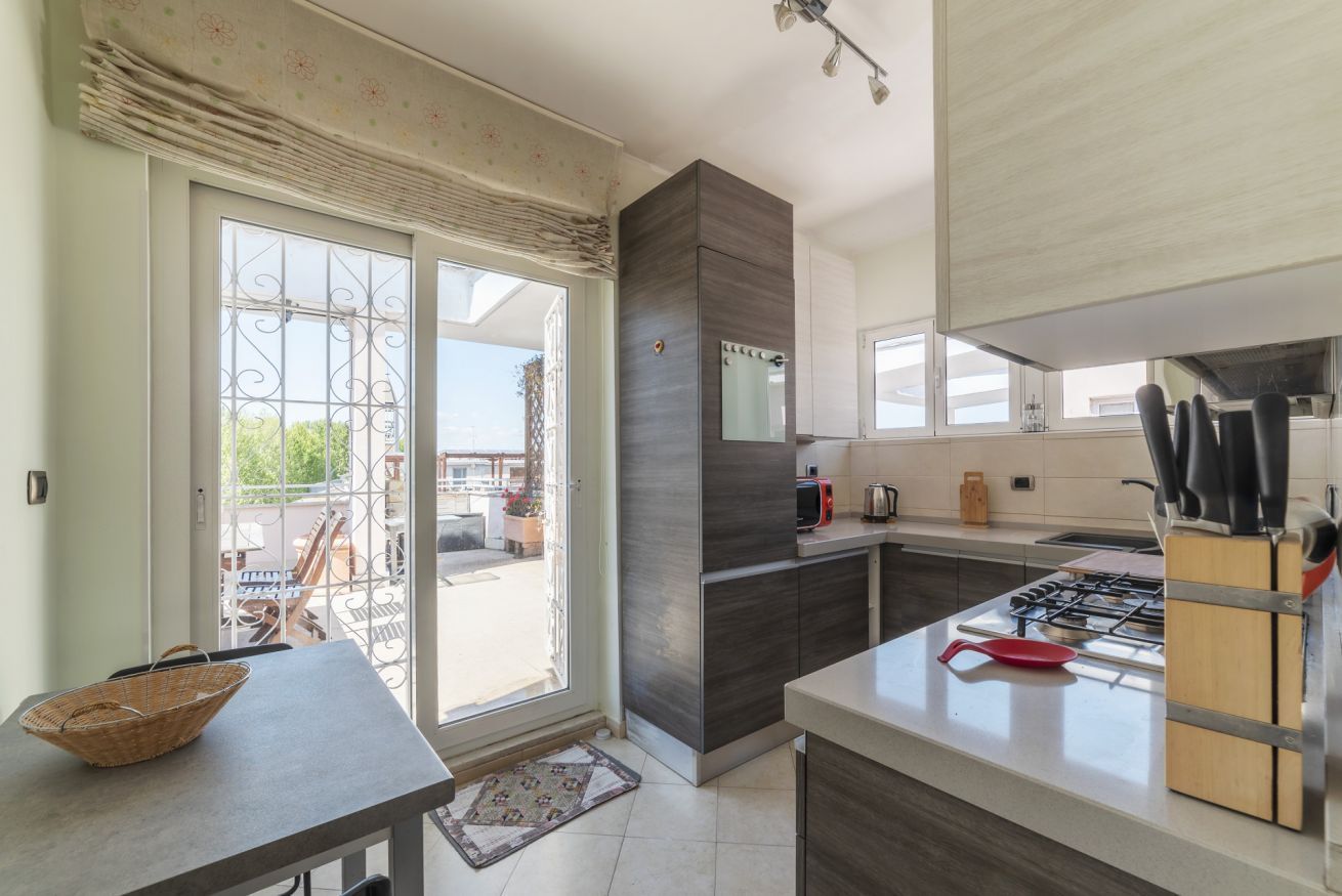 A modern kitchen with a gas stove, a microwave, and a sink. There is a dining area with a table and chairs visible through the sliding glass doors.
