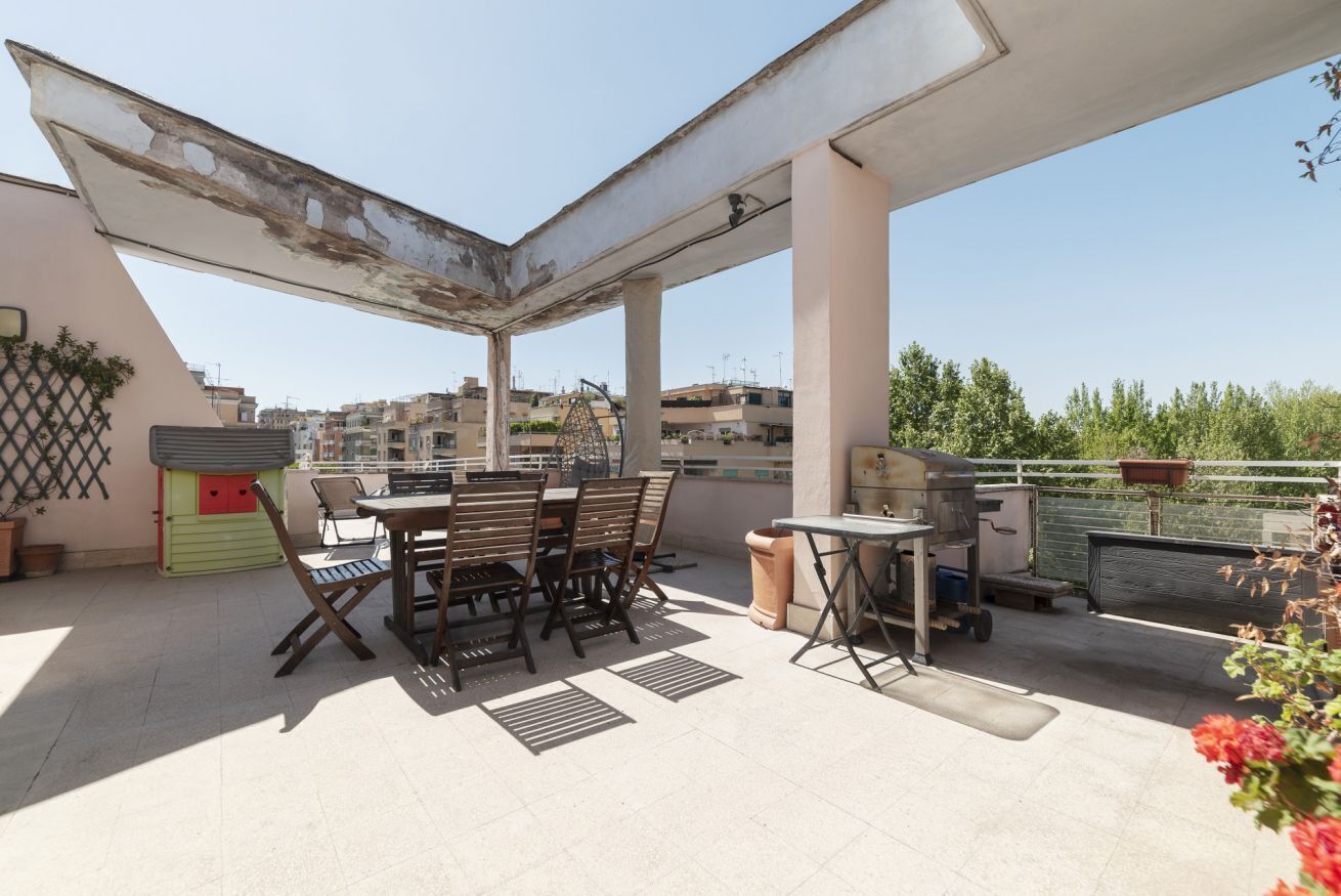 A rooftop terrace with a table and chairs, a grill, and a view of the cityscape.