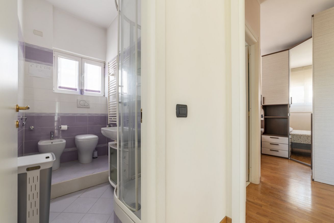 Baño con inodoro, bidé y lavamanos, ducha con puerta de cristal y suelo de madera.