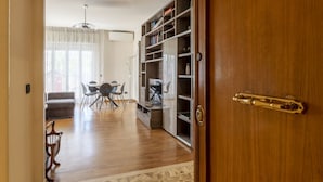 A room with a wooden floor, a dining table with chairs, a sofa, and a bookshelf. - GuestHost - Cozy and comfortable 75sqm apartment, able to accommodate up to 6 people, located on the 5th floor with elevator (not suitable for disabled peolple) of a building less than 10 minutes walk away from Bologna Metro stop and the homonymous squ (Roma)