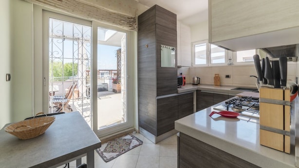 A modern kitchen with a gas stove, a microwave, and a sink. There is a dining area with a table and chairs visible through the sliding glass doors. - GuestHost - Cozy and comfortable 75sqm apartment, able to accommodate up to 6 people, located on the 5th floor with elevator (not suitable for disabled peolple) of a building less than 10 minutes walk away from Bologna Metro stop and the homonymous squ (Roma)