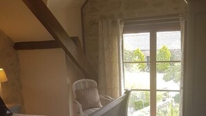 Un dormitorio con piso de madera, una cama, una silla y una ventana con vista a espacios verdes.