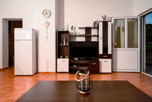 A modern living room with a flat-screen TV, a white refrigerator, and a wooden coffee table.