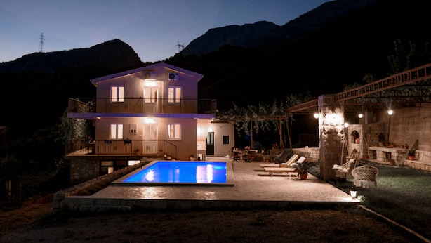Une maison à deux étages avec une piscine, un espace salon extérieur et un mur en pierre.