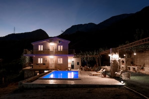 A two-story house with a swimming pool, outdoor seating, and a stone wall.