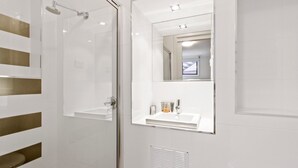Ein modernes Badezimmer mit einer gläsernen Dusche, einem weißen Waschbecken mit Spiegel darüber und einer Lüftungseinheit an der Wand.