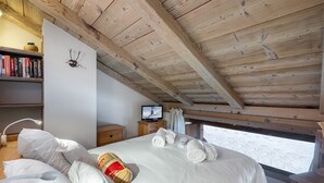 A bedroom with a wooden ceiling, a bed with white linens, a television on a wooden nightstand, and a bookshelf with books.
