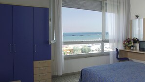 A bedroom with a bed, a desk, a chair, a wardrobe, and a window with a view of the sea. - Hotel Eritrea (Cesenatico)