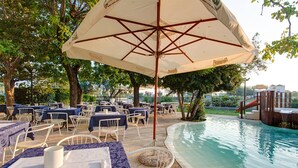 An outdoor pool area with tables and chairs, surrounded by trees and a pool. - Hotel Eritrea (Cesenatico)
