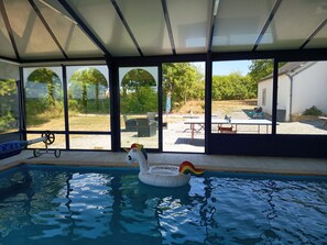 A swimming pool with a swan float, large windows, and outdoor seating.