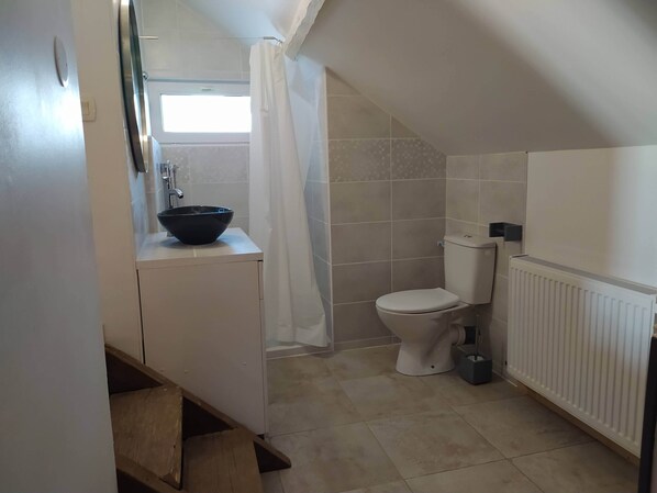 Un baño pequeño y funcional con lavamanos blanco, inodoro y zona de ducha.