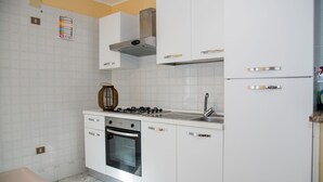 Ett kompakt kök med vita skåp, en gasspis, en ugn och en diskho i rostfritt stål.