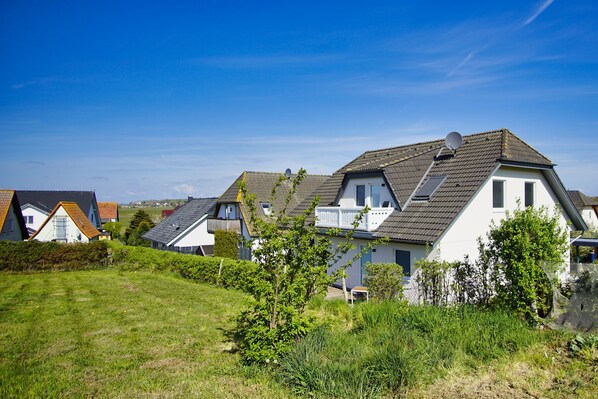 A row of houses with sloped roofs, a grassy area in the foreground, and a clear blue sky. - Haus Südperd Ferienwohnung Strandwinde (Mönchgut OT Thiessow)