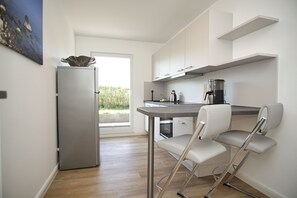 A modern kitchen with a refrigerator, coffee maker, and a dining area with a chair. - Haus Südperd Ferienwohnung Strandwinde (Mönchgut OT Thiessow)