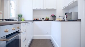 Et moderne køkken med hvide skabe, komfur i rustfrit stål og en bordplade med diverse køkkenartikler.