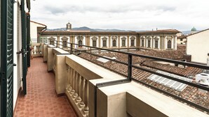 Ein Balkon mit Blick auf ein historisches Gebäude mit klassischer Architektur, einem Ziegeldach und einem fernen Gebirgszug.