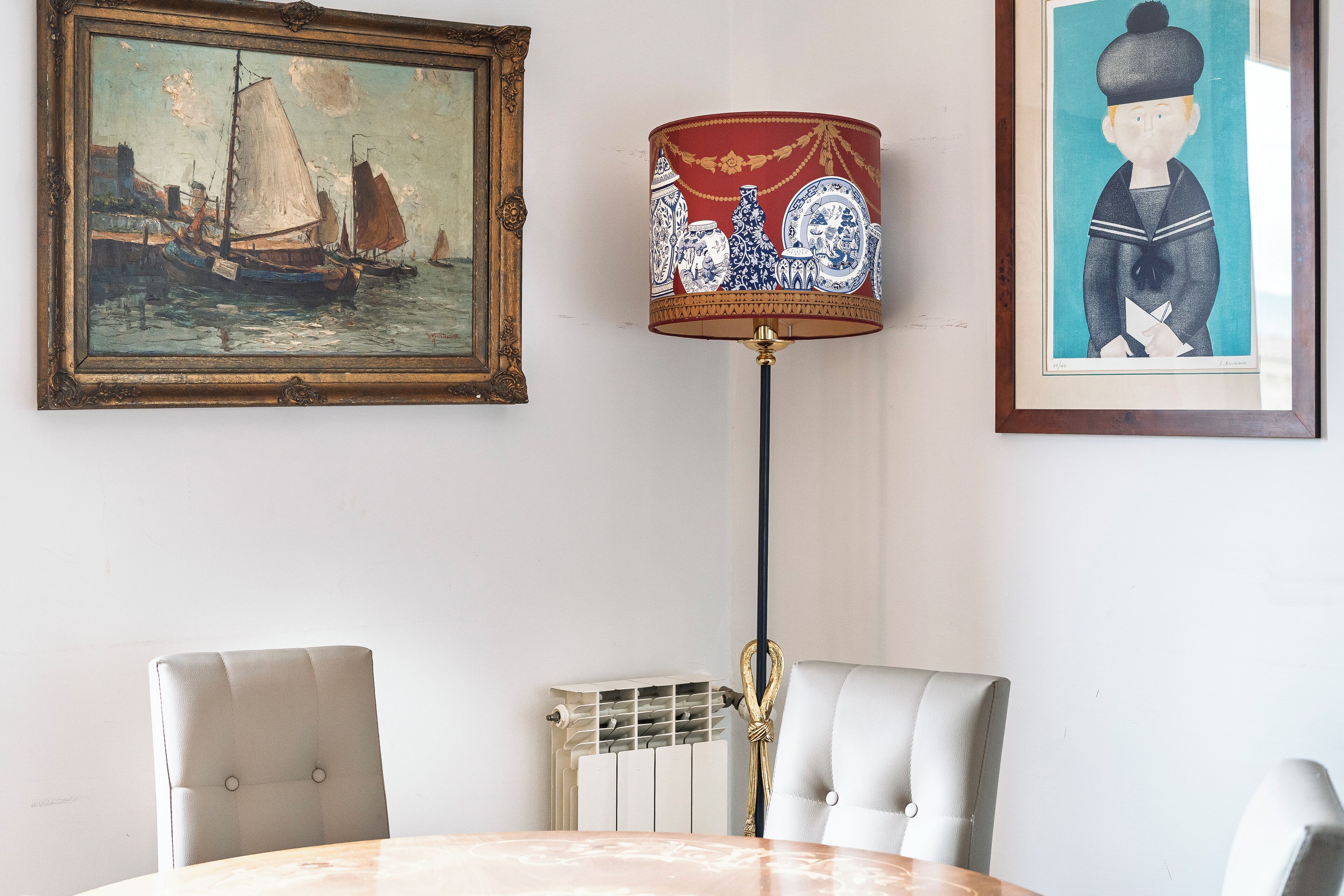 A dining area with a table, two chairs, a floor lamp, and two framed artworks on the wall.
