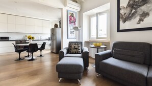 A modern living room with a grey sofa, a matching ottoman, and a dining area with black chairs. A large painting hangs on the wall, and there is a window providing natural light. - Matteotti Apartment - Two Bedroom Apartment, Sleeps 6 (Firenze)