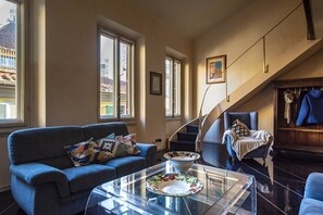 Een woonkamer met een bank, een glazen salontafel en een trap naar een hoger gelegen verdieping.