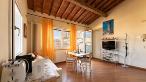 Een gezellige woonkamer met houten plafond, een eettafel met stoelen, een tv-meubel en een raam met gordijnen.