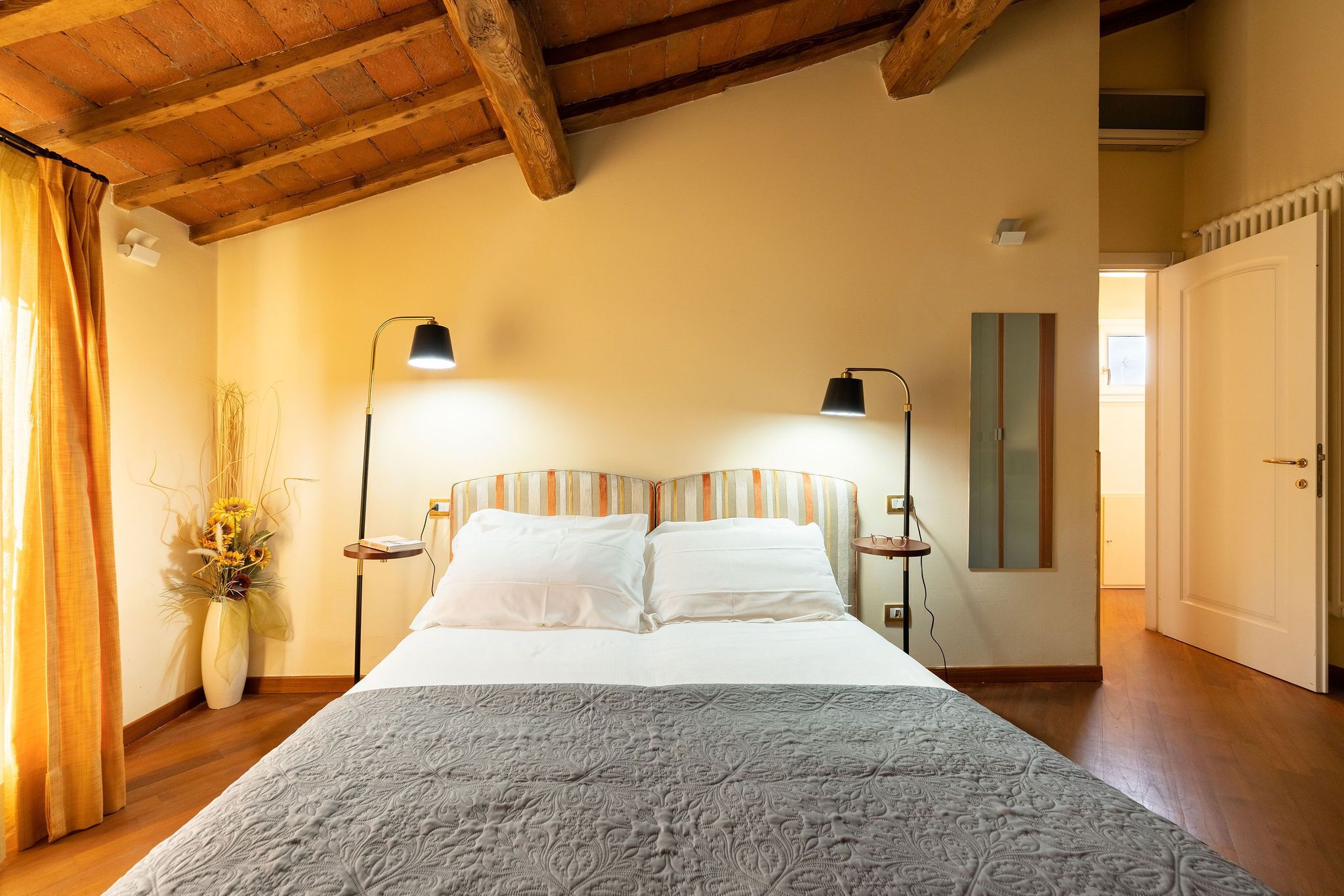 Un dormitorio con una cama grande, dos lámparas de noche, un florero con flores y techo de madera.