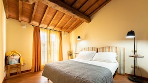 Een slaapkamer met een houten plafond, een bed met wit beddengoed, een bedlampje en een koffer op een klein tafeltje.