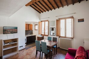A spacious living area with a dining table, chairs, a red sofa, and a kitchen in the background.