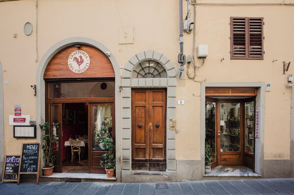 A building with a wooden archway entrance, a door, and a window with shutters. There are signs and a menu board outside.