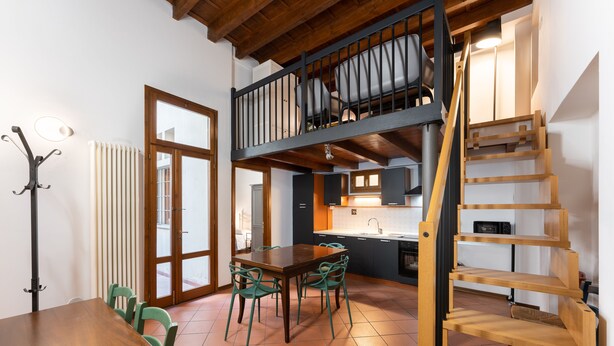 Ein Essbereich mit Holztisch und -stühlen, eine Küche mit Spüle und Schränken sowie eine Holztreppe.