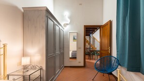 Ein Hotelzimmer mit einem Bett, einem Nachttisch mit Lampe, einem Kleiderschrank, einem blauen Sessel und Blick auf den Speisesaal.