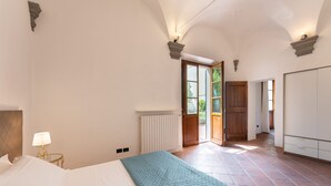 Een slaapkamer met een bed, een bedlamp, een radiator en uitzicht op een gang.