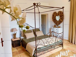 Un lit à baldaquin avec un cadre en métal, une table de chevet avec une lampe et un miroir décoratif accroché au mur.