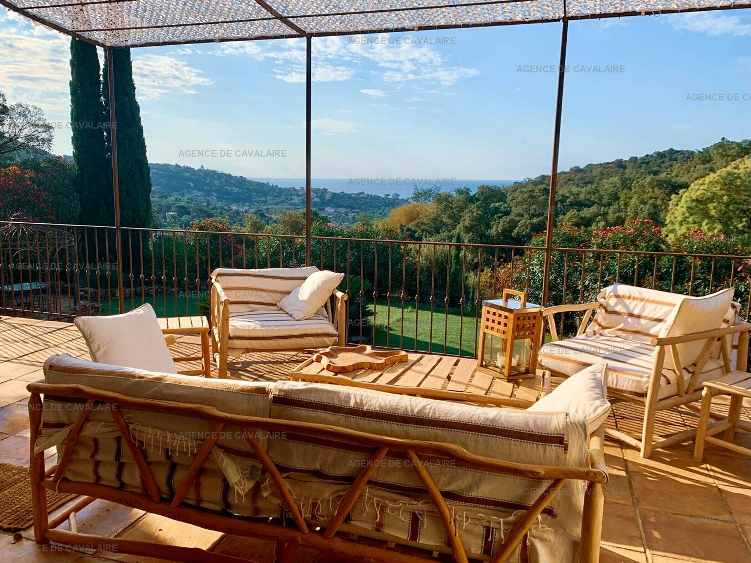 A covered outdoor seating area with wicker furniture and a view of a lush landscape.