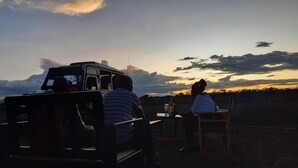 Un vehículo con una persona adentro, una mesa con una botella y un vaso, y una persona sentada en una silla.
