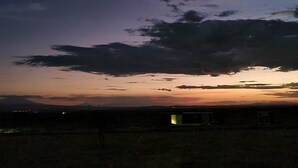 Paisaje rural al anochecer con una gran formación de nubes y un edificio pequeño en primer plano.