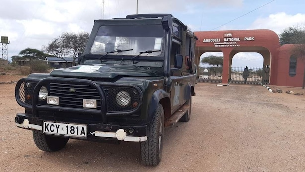 Un vehículo todoterreno negro con placa KCY 181A estacionado frente a la entrada del Parque Nacional de Amboseli.