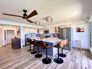A modern kitchen with a central island, bar stools, a ceiling fan, and a refrigerator.