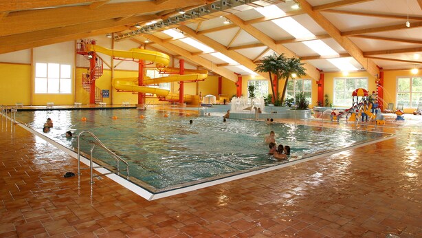 An indoor swimming pool with multiple lanes, a water slide, and a play area. - Sporthotel Neuruppin (Neuruppin)