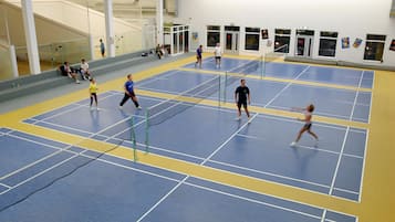 Un pabellón deportivo con varias canchas de tenis, zonas de asientos y una escalera.