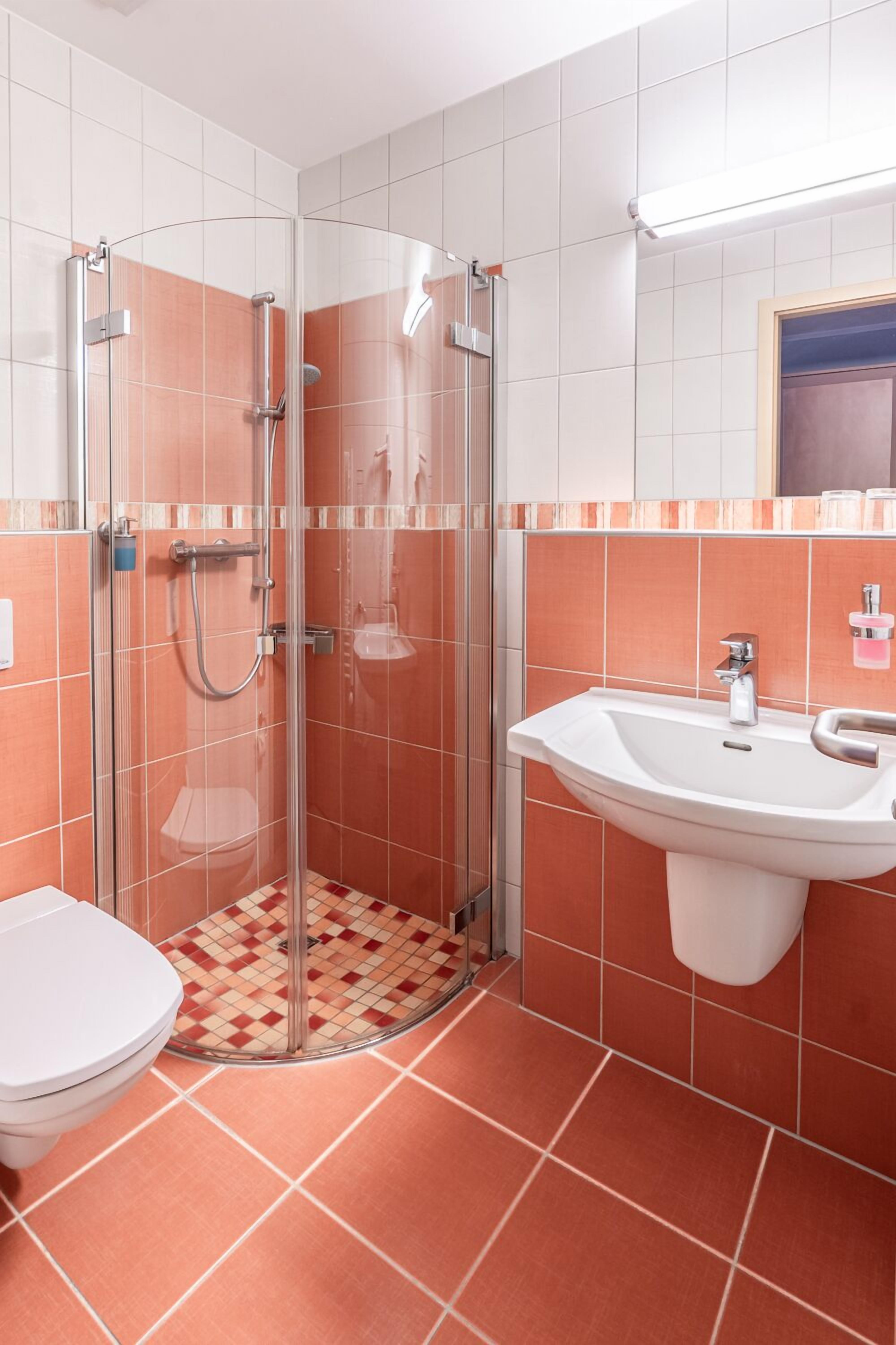 Een badkamer met een douchecabine van glas, een witte wastafel en een toilet.