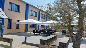 An outdoor seating area with tables and chairs, a small water feature, and umbrellas. - Sporthotel Neuruppin (Neuruppin)