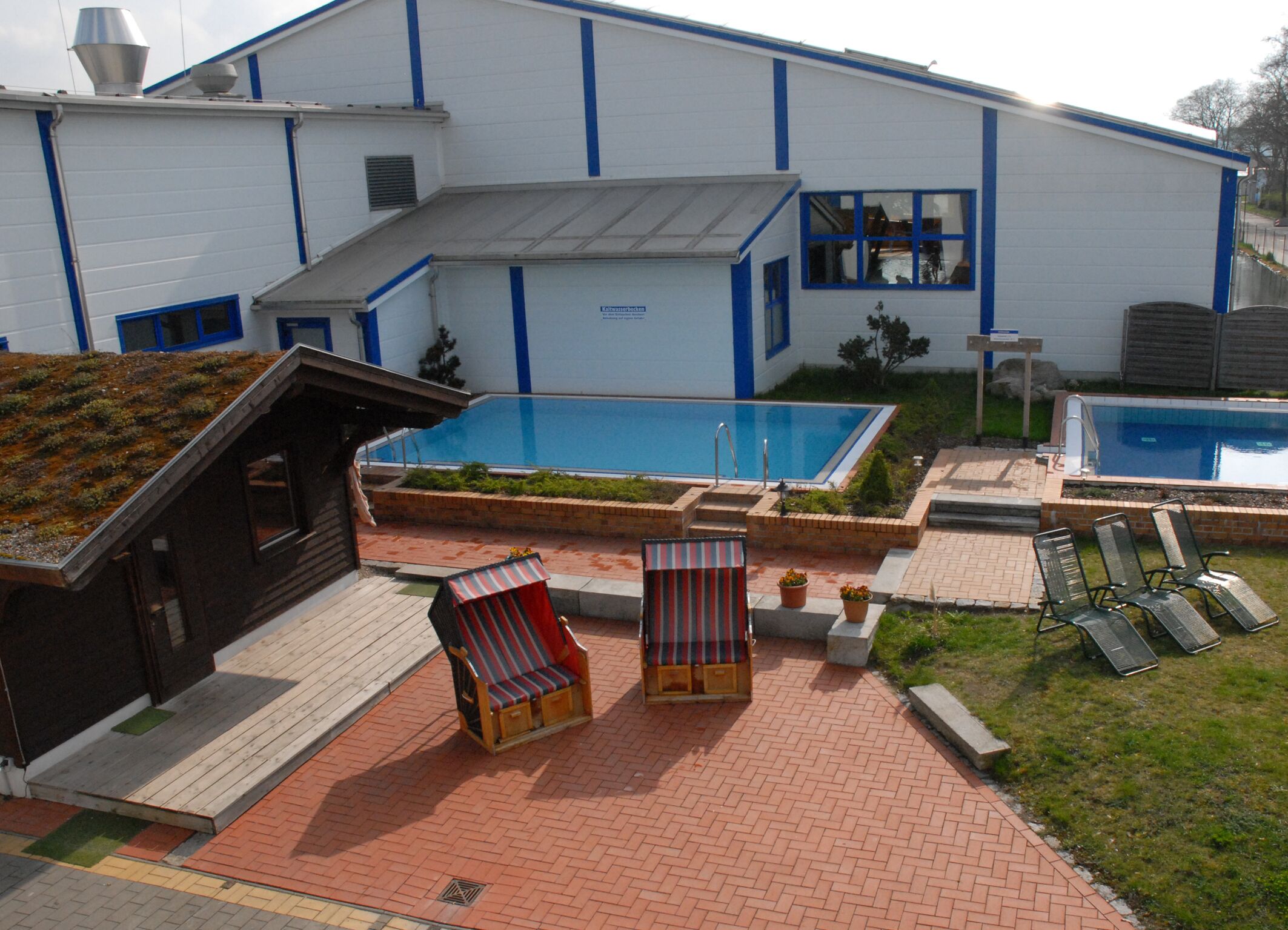 A modern building with a swimming pool, outdoor seating, and a small garden area.