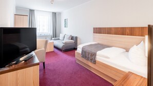 A hotel room with a bed, a TV, a desk, and a sofa. - Sporthotel Neuruppin (Neuruppin)