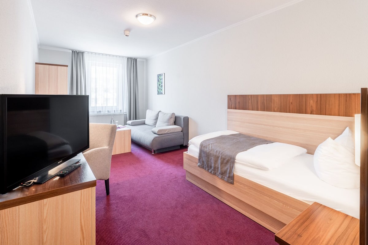 A hotel room with a bed, a TV, a desk, and a sofa.