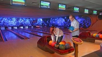 A bowling alley with multiple lanes, a woman preparing to bowl, and a man holding a bowling ball.