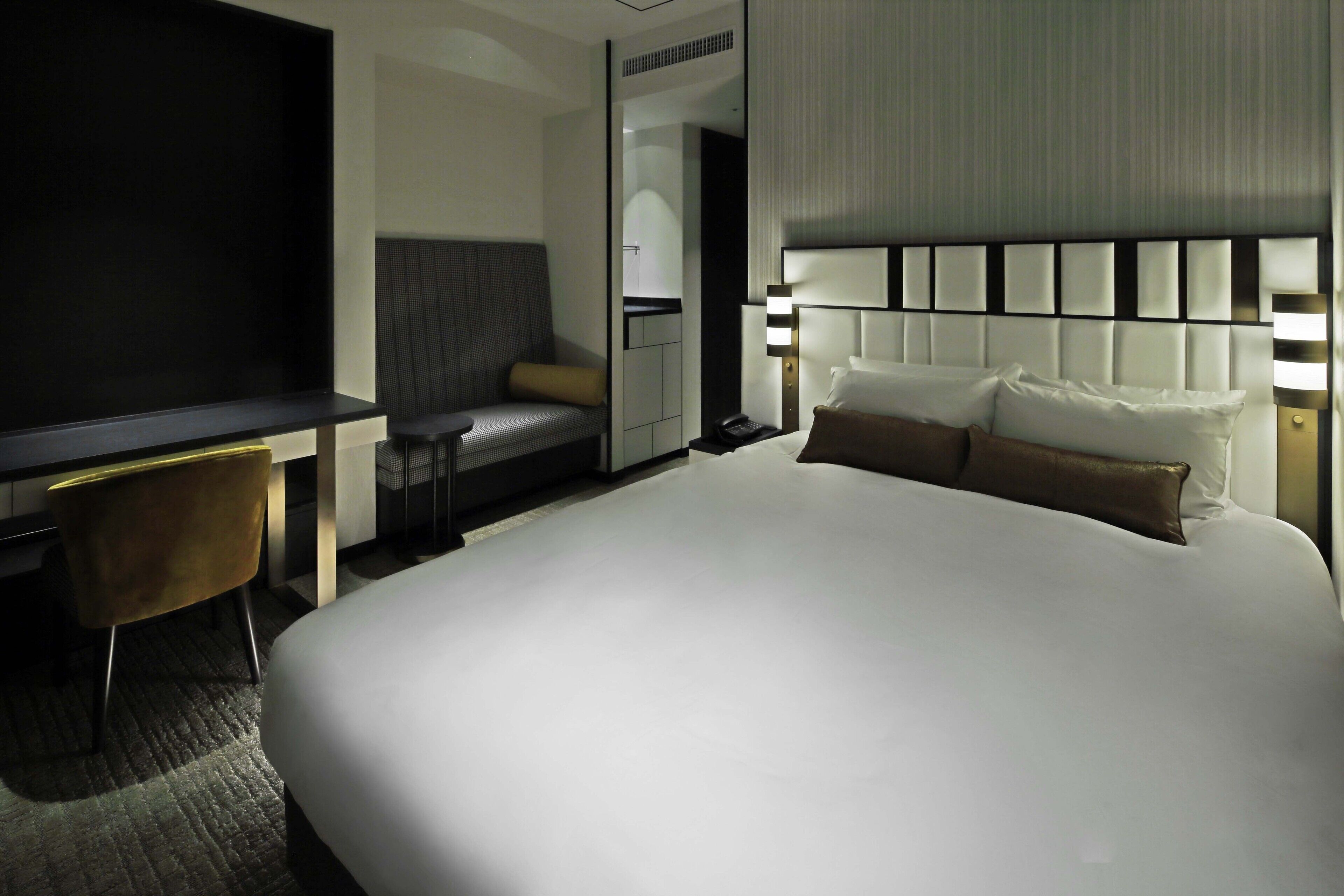 A hotel room with a large bed, a desk, a chair, and a bedside table.