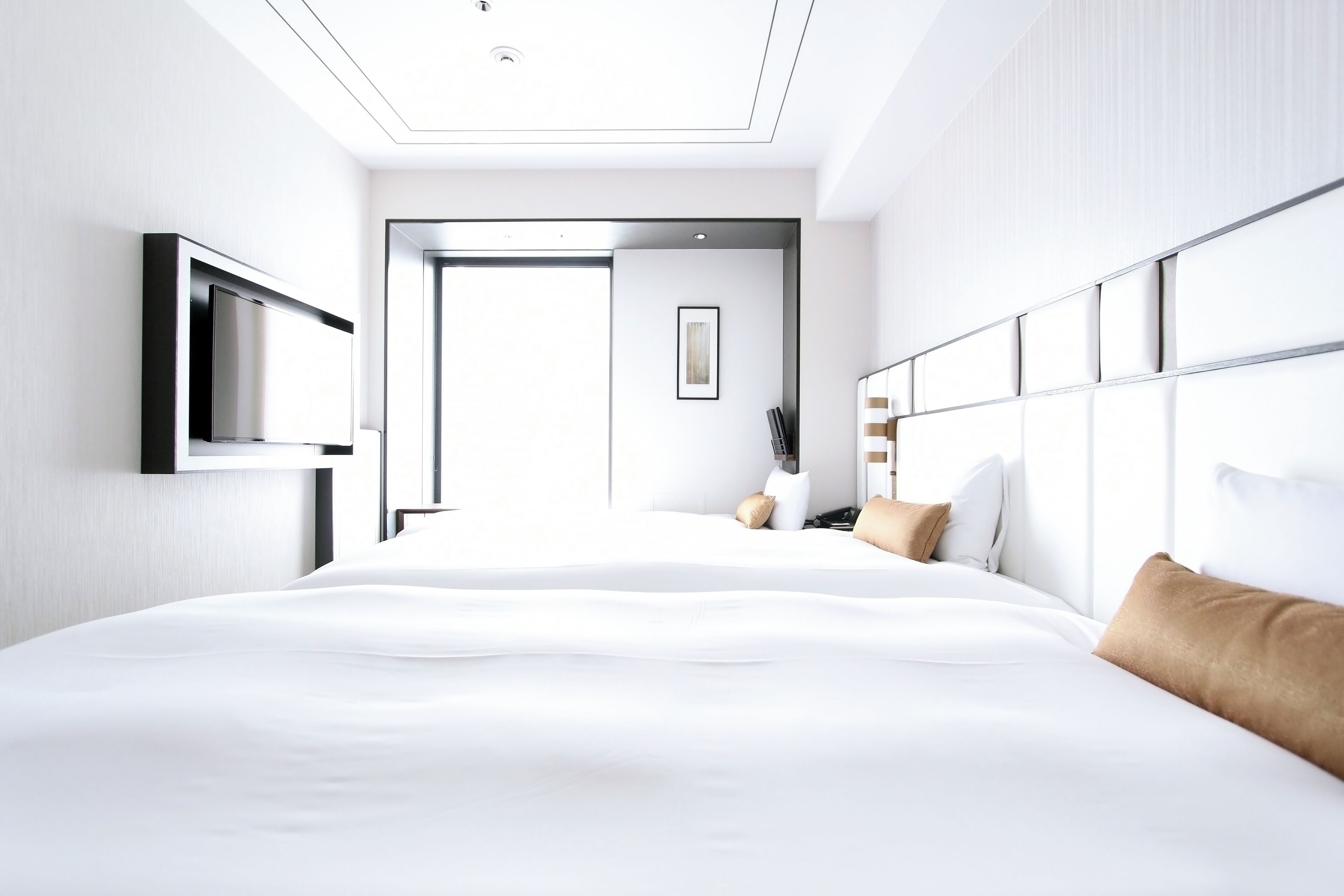 A modern hotel room with a large bed, a flat-screen TV mounted on the wall, and a bedside table with a lamp.